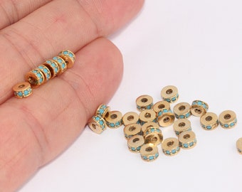 May include: A close-up of a pile of gold-colored spacer beads with turquoise-colored stones. The beads are round and have a hole in the center. The beads are on a white surface.