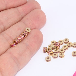 Peut inclure: Gros plan sur un tas de perles d'espace dorées avec des strass roses. Les perles sont éparpillées sur une surface blanche à côté d'une règle rose.