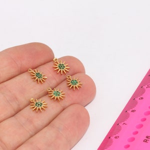 May include: Five gold-coloured sun charm pendants with green crystal accents. The charms are small and delicate, perfect for adding a touch of sparkle to jewellery projects.