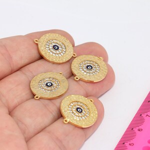 May include: Four gold-toned metal charms with a blue evil eye design and clear rhinestones. The charms have two holes for attaching to jewelry.