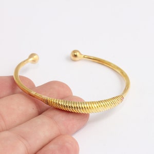 May include: A gold-toned bangle bracelet with a textured, ribbed design. The bracelet has rounded ends.