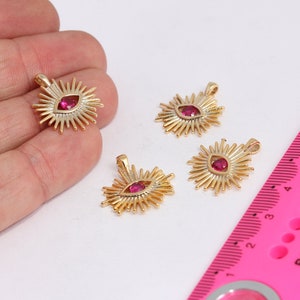 Könnte beinhalten: Vier goldfarbene Anhänger mit einem roten Edelstein in der Mitte, umgeben von einem Sonnenstrahlendesign. Die Anhänger befinden sich auf einer weißen Oberfläche.