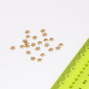 May include: A scattering of small gold star-shaped embellishments on a white surface, next to a yellow ruler.