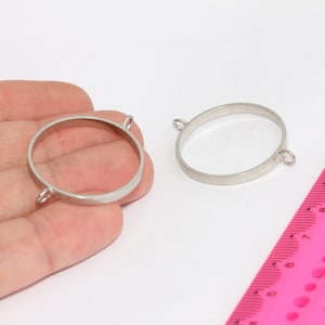 Op de afbeelding: Twee zilveren metalen ringblanken met springringen. De ringen zijn ongeveer 2,5 cm in diameter. Een roze liniaal is op de achtergrond.