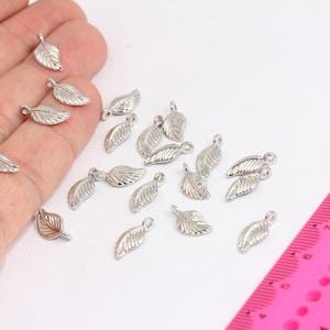 Könnte beinhalten: Eine Sammlung von silbernen Blattanhängern, perfekt für die Schmuckherstellung oder Bastelprojekte. Die Anhänger sind etwa 2,5 cm lang und haben ein zartes Blattdesign.
