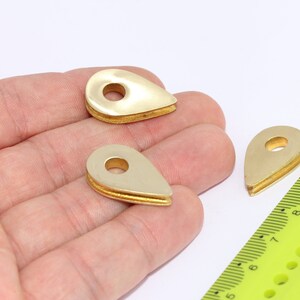 May include: Three gold-colored metal teardrop-shaped rings with a hole in the center. The rings are about 1 inch long and are sitting on a hand.