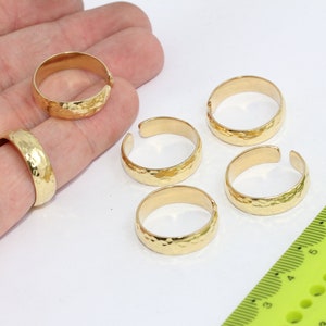 May include: Five gold-toned hammered metal rings. The rings are open and adjustable. The rings are displayed on a hand and a ruler.