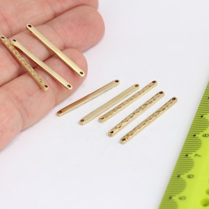 Puede incluir: Siete conectores de barra de metal de color dorado con dos agujeros cada uno. Las barras son lisas y texturizadas. Una regla está en el fondo.