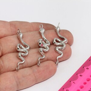 Può includere: Tre ciondoli a forma di serpente argentati con un designo a spirale. I ciondoli sono appesi ad anelli a salto.