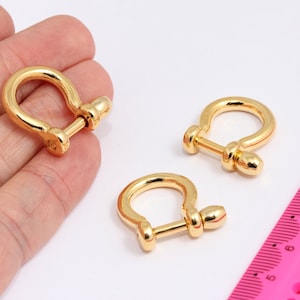 Könnte beinhalten: Drei goldfarbene D-Ringe aus Metall mit Stiftverschluss. Die D-Ringe haben einen Durchmesser von etwa 2,5 cm.