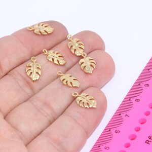 Könnte beinhalten: Acht goldfarbene Metall-Anhänger in Form von Monstera-Blättern mit einer Öse oben zum Anbringen an Schmuck oder andere Bastelarbeiten.