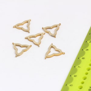 Pode incluir: Cinco pingentes de metal de forma triangular de cor dourada com um design intrincado. Os pingentes têm um furo em cada ponto para serem presos a joias ou outros trabalhos manuais.