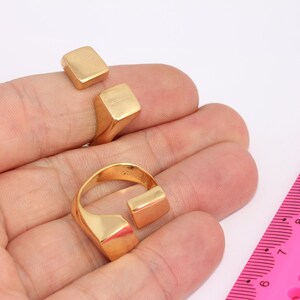 May include: Three gold-toned rings with geometric designs. The rings are stacked on a hand, with the largest ring on the bottom and the smallest ring on top.