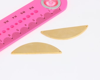 Puede incluir: Dos formas de metal de color dorado en forma de semicírculo con agujeros a cada lado. Las formas tienen un diámetro de aproximadamente 5 cm y están sobre una superficie blanca.
