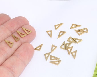 May include: A close-up of a hand holding a pile of small, gold-colored triangle-shaped metal charms. The charms are about 1/2 inch in size and have a hollow center. There is a ruler in the background.