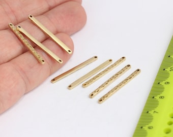 May include: Seven gold-coloured metal bar connectors with two holes each. The bars are smooth and textured. A ruler is in the background.