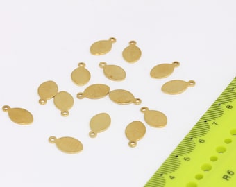 May include: A group of 14 gold-colored metal oval-shaped charms with a small loop at the top. The charms are scattered on a white surface.