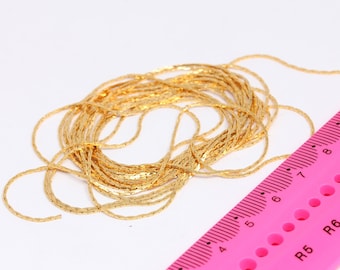 May include: A close-up of a gold chain, coiled and arranged in a circular shape. A pink ruler with black markings is partially visible in the background.