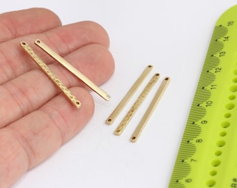 May include: Five gold-coloured metal bar connectors with a hammered texture and two holes at each end. The bars are arranged in a row on a white surface with a green ruler in the background.