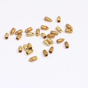 May include: A group of 20 gold-colored metal caps with a small hole in the top. The caps are scattered on a white surface.