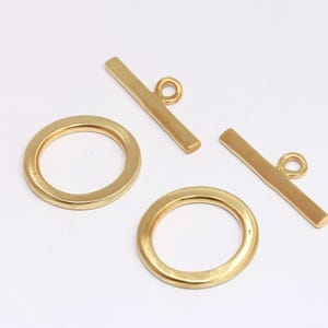 May include: Two gold-toned metal toggle clasps with round rings. The clasps are made of a smooth, shiny metal.