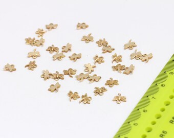 May include: A scattering of gold-colored metal dragonfly charms on a white surface. The charms are small and delicate, with intricate details.