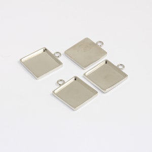May include: Four silver-toned square pendant trays with a loop at the top for hanging. The trays are designed to hold small items, such as resin or other crafts.