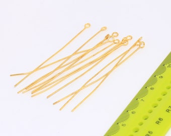 May include: A group of 10 gold-coloured head pins with loops on one end. The pins are approximately 5 cm long and are arranged in a random pattern on a white surface.