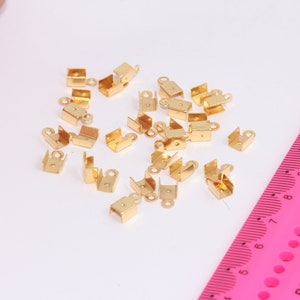 Puede incluir: Un montón de cierres de metal de color dorado para la elaboración de joyas. Los cierres son pequeños y tienen un bucle en un extremo.