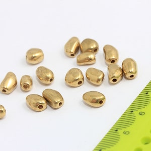 May include: A collection of 16 gold-coloured metal beads, each with a hole in the centre. The beads are oval-shaped and have a slightly textured surface.
