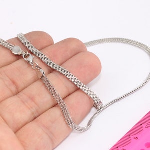 Könnte beinhalten: Eine silberne Kettenkette mit einem Karabinerverschluss. Die Kette besteht aus mehreren Strängen kleiner, miteinander verbundener Metallteile. Die Kette liegt auf einer Hand und einem rosa Lineal.