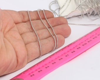 May include: A silver snake chain necklace laid out on a hand, with a pink ruler marked with numbers R2 through R13 in the foreground.