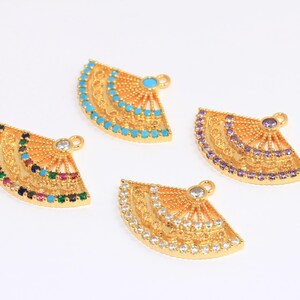 Könnte beinhalten: Vier goldfarbene Fächer-Anhänger mit bunten Kristallverzierungen. Jeder Anhänger hat ein anderes Farbschema: Türkis, Lila, Weiß und mehrfarbig.