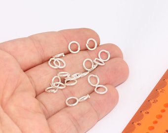 May include: A close-up of a hand holding a pile of silver jump rings. The rings are small and round, and they are perfect for jewelry making.