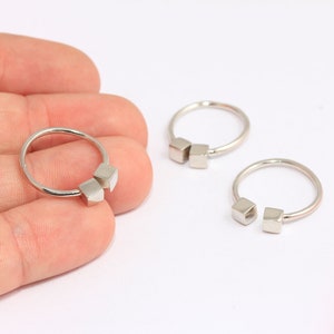 Op de afbeelding: Drie zilveren ringen met vierkante accenten. De ringen zijn aan één kant open en hebben een minimalistisch ontwerp.