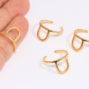 May include: Four gold-toned rings with a simple, open, rounded, rectangular shape. The rings are made of metal and have a smooth finish.