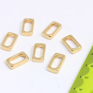 May include: Seven gold-coloured metal rectangular jump rings with a rounded edge. The jump rings are approximately 2.5 cm long and 1.25 cm wide.