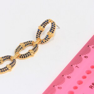May include: Gold tone earrings with three linked oval shapes, each set with blue stones.