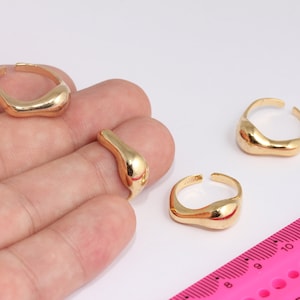 Op de afbeelding: Drie gouden ringen met een unieke, onregelmatige, organische vorm. De ringen worden op een hand getoond tegen een witte achtergrond.