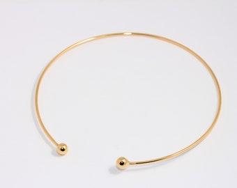 May include: A gold choker necklace with two small round balls at the ends.