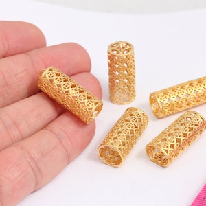 May include: Five gold-coloured metal tubes with an intricate, openwork design. The tubes are approximately 2.5 cm in length.