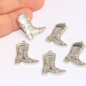 Könnte beinhalten: Fünf silberne Cowboy-Stiefel-Anhänger mit Sternenmuster. Die Anhänger sind etwa 5 cm hoch.