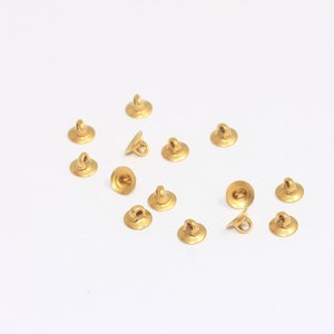 May include: A group of 14 gold-toned metal loop and cup bead caps. The bead caps are scattered on a white surface.