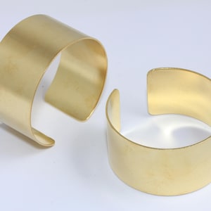 Puede incluir: Dos pulseras de metal de color dorado. Las pulseras son simples y tienen un acabado liso y pulido.
