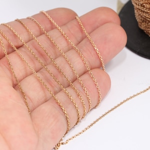 May include: A close-up of a gold chain, shown in multiple strands, on a hand. The chain is a delicate, cable style.