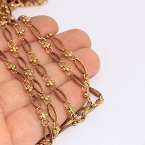 Puede incluir: Cadena de oro con eslabones ovalados y pequeñas cuentas redondas. La cadena está colocada sobre una mano, con una regla en el fondo.