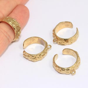 May include: Four gold-tone metal rings with a textured surface. Each ring has a small loop on one side.