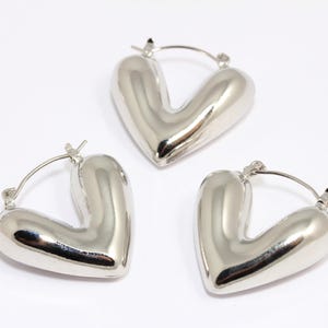 Può includere: Tre orecchini a cerchio a forma di cuore in argento. Gli orecchini sono lisci e lucidi.