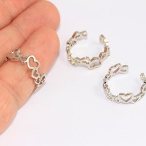 Puede incluir: Dos anillos de plata con un diseño en forma de corazón. Los anillos son abiertos y ajustables.
