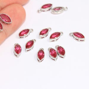 May include: A collection of 12 silver-toned marquise-shaped charms with red crystal accents. Each charm has a loop for attaching to jewelry or other crafts.